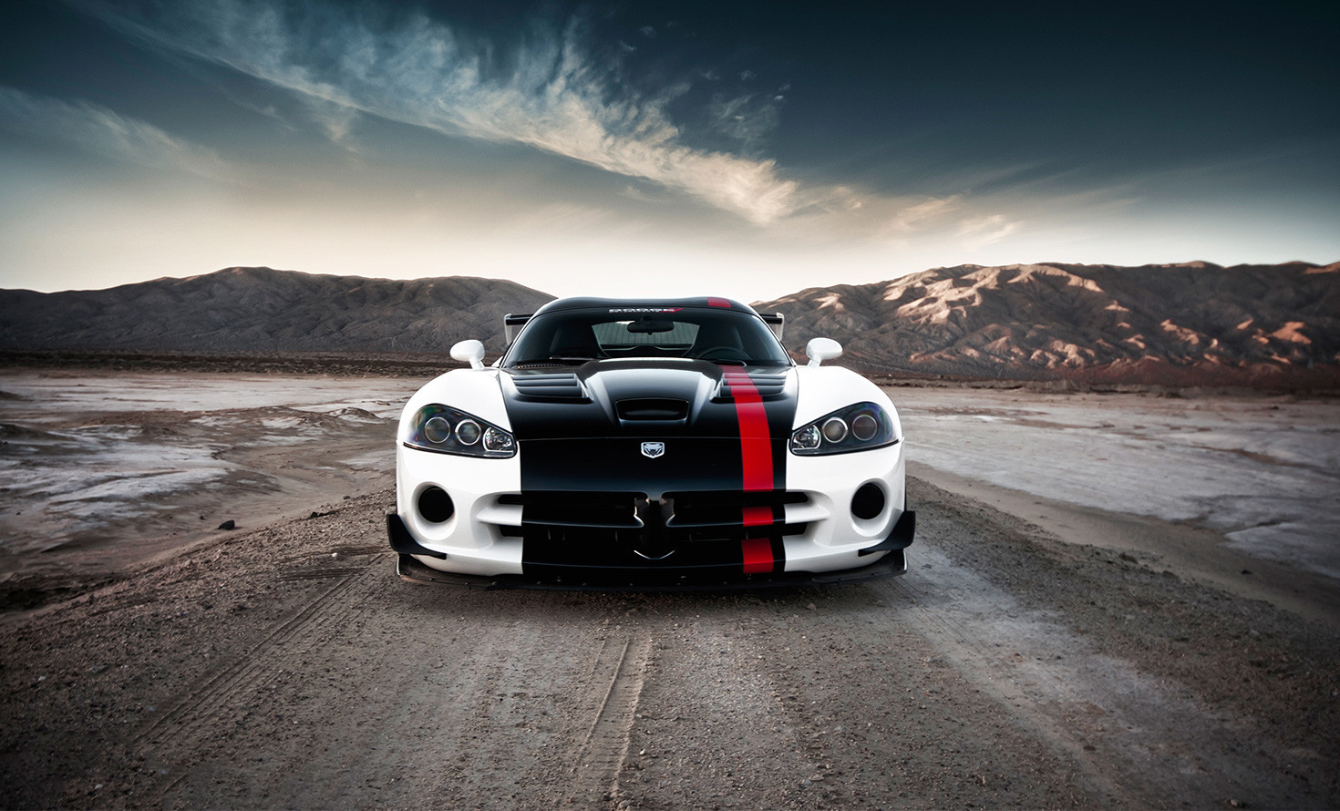 White sports car with black and red stripes on a desert road under a dramatic sky.