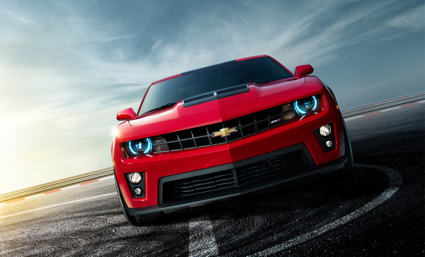 Red sports car on a race track at sunset, showcasing front view and glowing headlights.