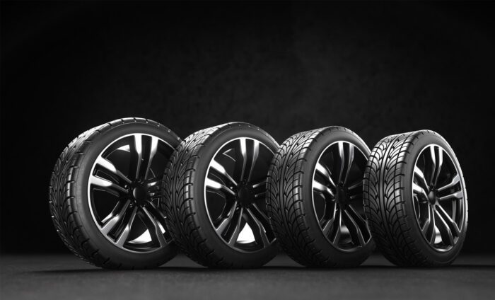 Four high-performance car tires on black background, showcasing sleek black rims and detailed tread patterns.