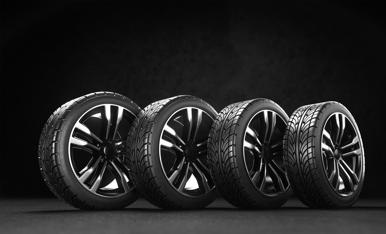 Four high-performance car tires on black background, showcasing sleek black rims and detailed tread patterns.
