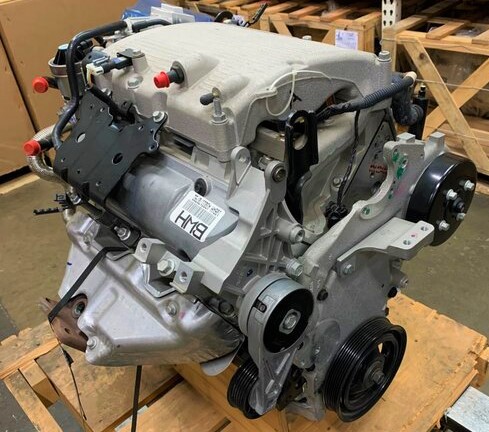 Car engine on wooden pallet in a workshop, showcasing mechanical components and design details.